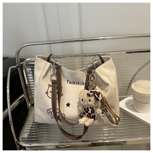 Close-up of beige canvas tote bag with cat prints and cute plush charm on a display shelf