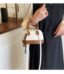 Detail of a chic two-tone shell bag with white and brown leather and tassel charm