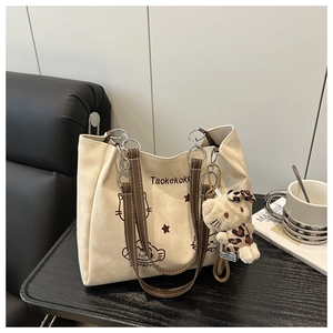 Detail of canvas tote bag featuring cat prints and a plush charm on a wooden table