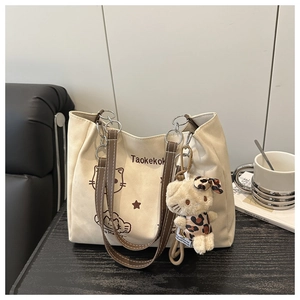 Close-up of canvas tote bag with brown leather handles and cute cat pendant detail