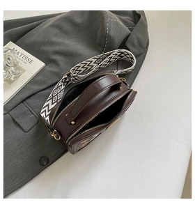 Detail of dark brown leather crossbody bag with geometric woven strap and zipper closure