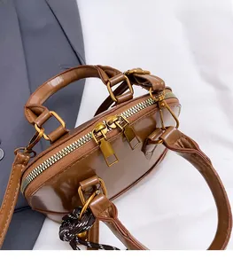 Close-up of golden dual-zipper hardware on brown glossy shell handbag with woven charm
