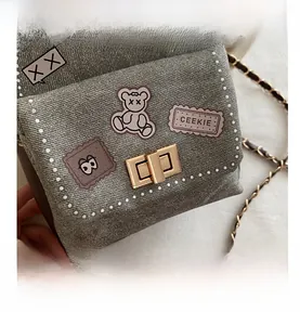 Close-up of grey denim mini crossbody bag with cartoon patches and gold twist-lock closure
