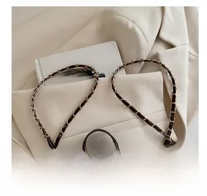 Detail of woven gold chain strap on a trendy crossbody bag over a beige blazer