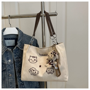 Detail of beige canvas tote bag with cat print, metal chain handles, and plush charm