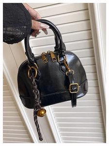 Detail of glossy black handbag with golden dual zippers and woven cord charm