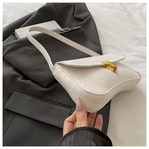 White baguette bag with crocodile texture and gold metal twist lock on a black suit