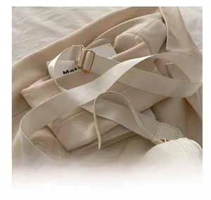 Détail de la large bandoulière en tissu et des finitions dorées sur le petit sac blanc