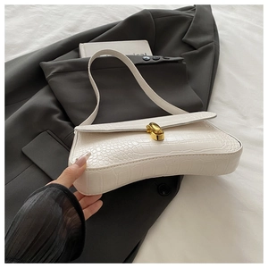 Detail of white crocodile-embossed leather underarm bag with gold metal clasp on a blazer