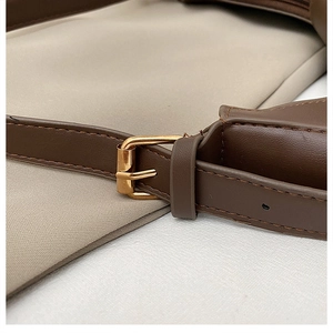 Detail of brown leather strap and golden metal buckle on beige canvas shoulder bag