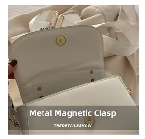 Détail de la boucle métallique magnétique dorée sur un sac à bandoulière en cuir blanc