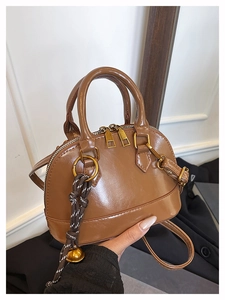 Détail d'un sac à main marron brillant avec finitions dorées et breloque clochette