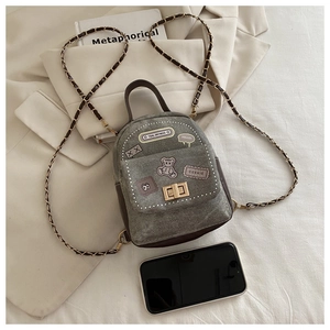 Detail of mini denim backpack featuring cartoon bear patches and leather woven chain