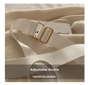 Détail de la bandoulière réglable en tissu blanc avec boucle dorée pour le sac