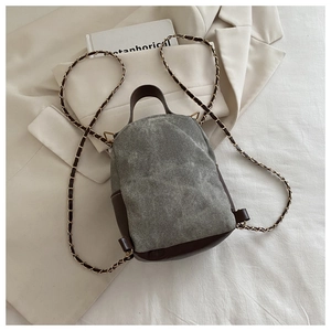 Detail of mini canvas backpack featuring brown leather accents and gold chain straps