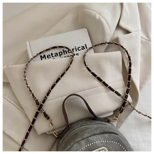 Detail of grey denim round crossbody bag with white stitching on chic white blazer