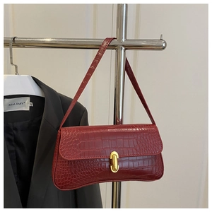 Close-up of deep red crocodile-embossed leather texture and gold metal buckle on baguette bag