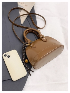 Détail d'un sac coquille marron brillant avec pendentif doré et bandoulière réglable