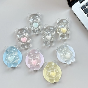 Transparent bear phone socket grips with plush colorful hearts on a desk surface