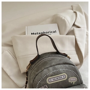 Detail of grey denim backpack with Tidal Dryness patches and golden chain strap