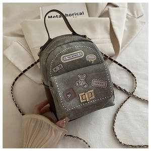 Detail of grey-green denim mini backpack with cartoon patches and golden twist lock closure