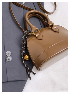 Détail d'un sac à main marron verni avec pendentif cloche dorée et gland à nœud