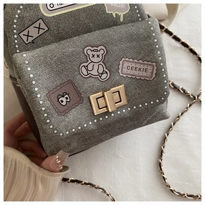Detail of taupe distressed denim bag with cartoon patches and metal twist lock