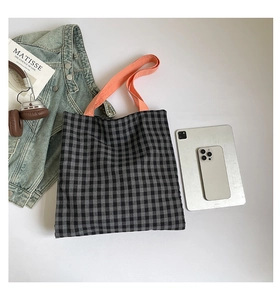 Gros plan d'un sac cabas à carreaux noir et blanc avec anses orange et accessoires quotidiens