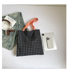 Vue à plat d'un sac cabas à carreaux avec anses orange et accessoires de mode décontractés