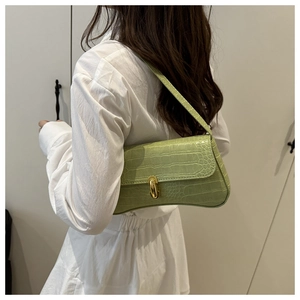 Detail of light green crocodile embossed baguette bag with golden buckle on model shoulder
