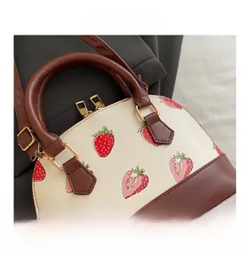 Vue détaillée du sac à main à motif fraise avec bordure en cuir brun et dorures