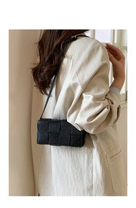 Detail shot of black woven leather square bag with thin shoulder strap on model side