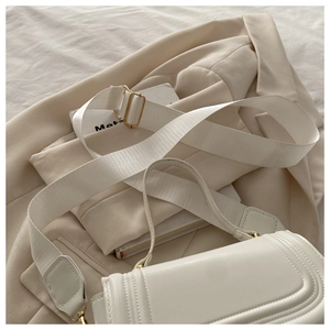 Gros plan d'un sac carré en cuir blanc avec large bandoulière en tissu et boucles dorées