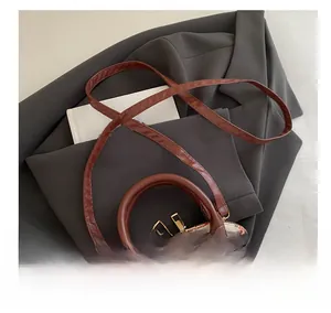 Détail de la bandoulière en cuir marron et de la poignée du sac à main aux fraises