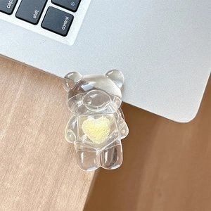 Macro detail of transparent bear phone grip featuring a yellow heart on a laptop surface