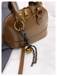 Détails d'un sac shell brillant marron avec fermetures dorées et pendentif clochette