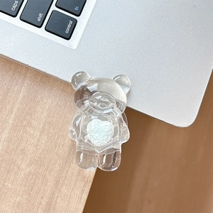 Detail of transparent bear phone grip with plush white heart on laptop background