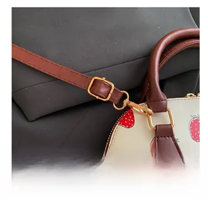 Détail de la bandoulière réglable et boucle en métal doré sur le sac à imprimé fraise