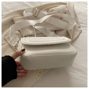 Détail du sac carré en cuir blanc avec large bandoulière en nylon sur fond beige
