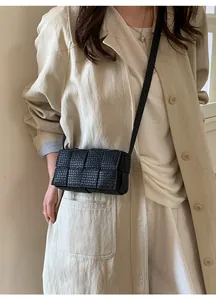 Detail of black woven leather crossbody bag worn over a beige trench coat for a stylish look