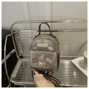Detailed shot of gray denim mini bag featuring embroidered patches and golden chain