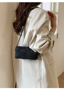 Detailed view of black woven crossbody bag with leather strap on beige trench coat