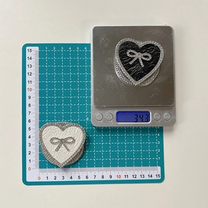 Detalle de soporte corazón para móvil con strass y lazo, muestra peso 34,3g y medida 5,5cm