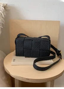Detail of black woven crossbody bag with matte texture and gold buckle on a wooden table