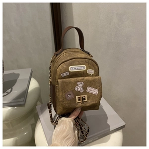 Macro detail of brown canvas mini backpack with vintage patches and luxury metal chain