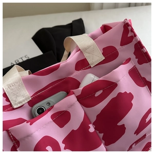 Detail of pink canvas tote with outer pockets holding a phone and earphone case