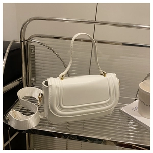 Détail d'un sac à main blanc avec large bandoulière et ferrures dorées sur étagère