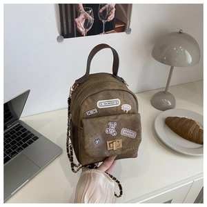 Mini brown crossbody bag featuring trendy patches and a gold chain strap on a desk