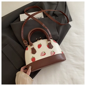 Detail of strawberry print crossbody bag with gold hardware on grey suit fabric