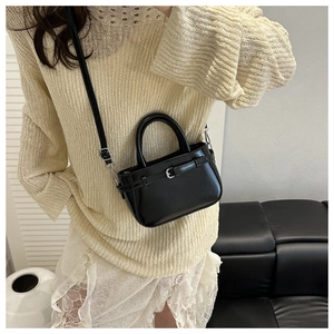 Model wearing a black glossy bucket bag with adjustable buckle in a minimalist home setting